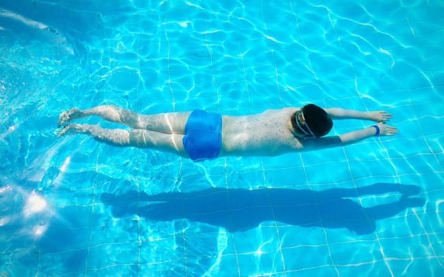 Un hombre bucea mientras practica natación en una piscina. Un hombre bucea mientras practica natación en una piscina.