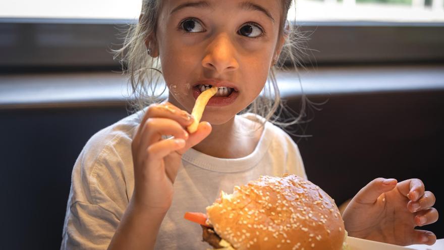 Una niña come una hamburguesa y patatas fritas sin sorpresas desagradables.