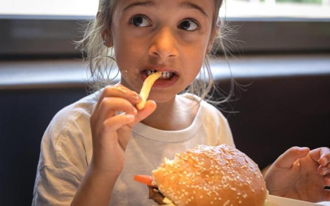 Una niña come una hamburguesa y patatas fritas sin sorpresas desagradables.