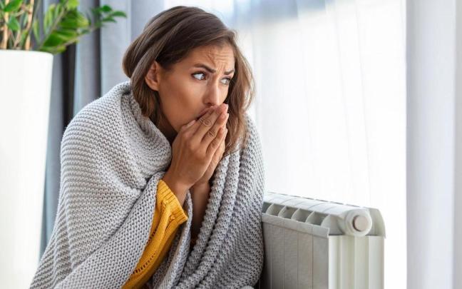 Una mujer con escalofríos intenta entrar en calor junto a un radiador.
