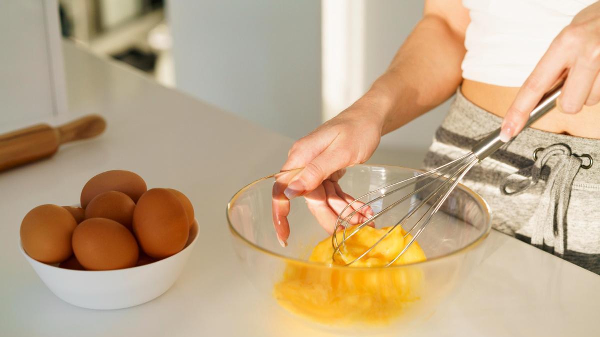 Manos de una chica mientras bate huevos para preparar una receta.