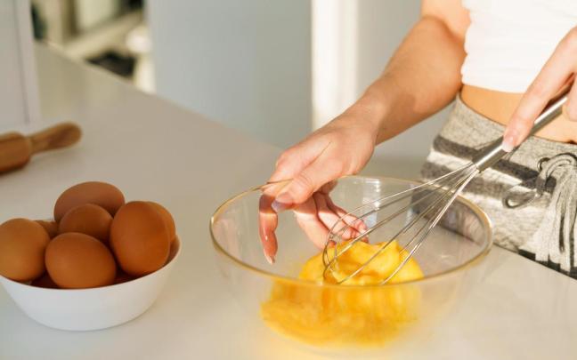 Manos de una chica mientras bate huevos para preparar una receta.
