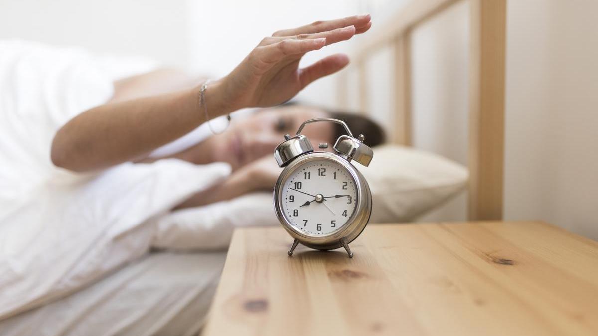 Chica apaga el despertador por la mañana nada más levantarse.