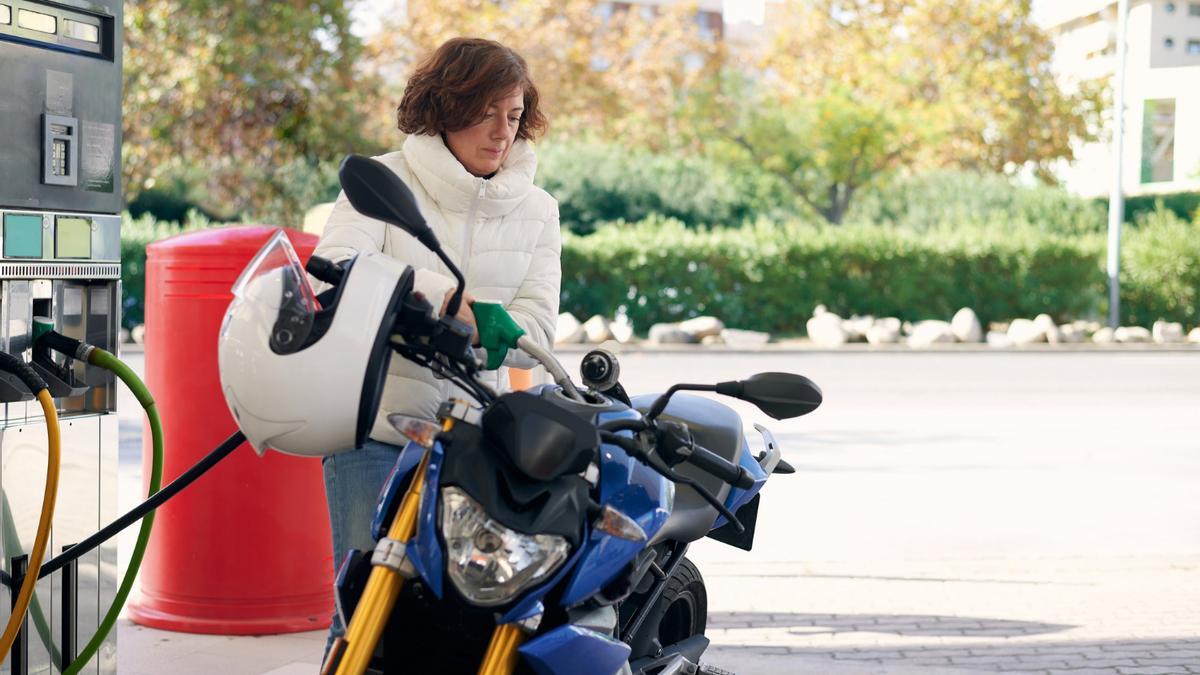 Una mujer reposta gasolina en su moto.