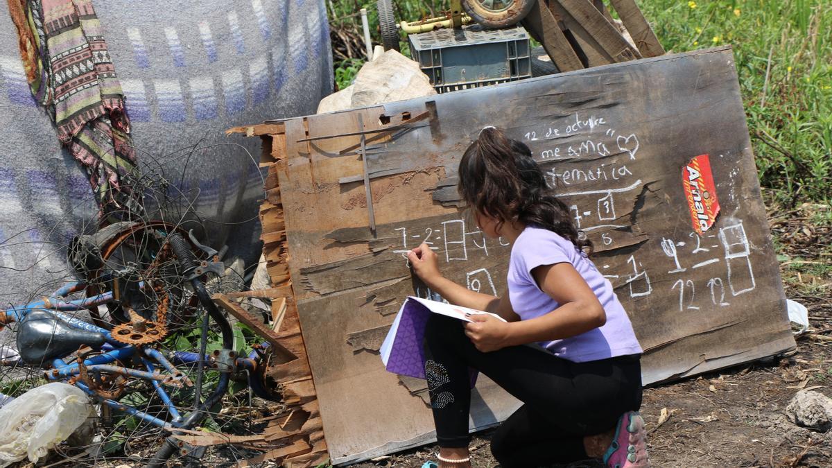 Una niña utiliza una madera vieja como pizarra para realizar su deberes de matemáticas.
