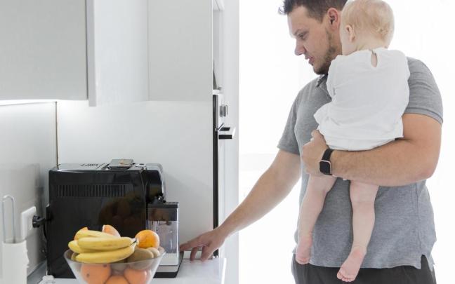 Un hombre con su bebé en brazos frente a un microondas.