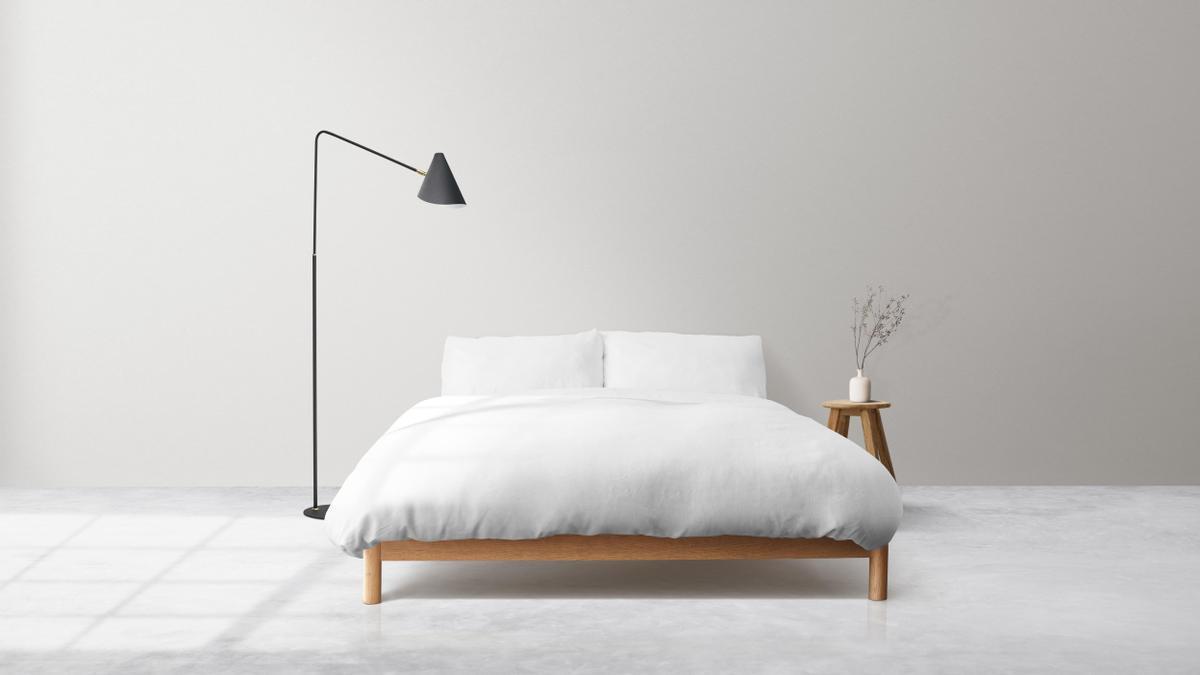 Dormitorio minimalista formado por una cama, una lámpara y una pequeña mesilla.