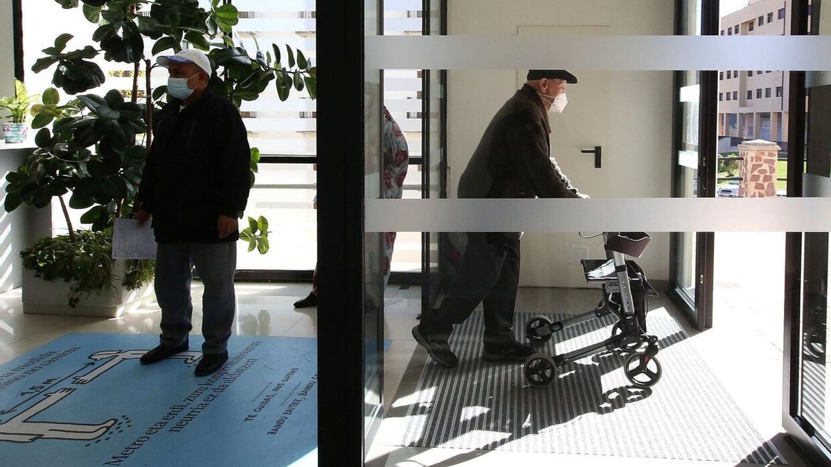 Un hombre de edad avanzada sale de un centro de salud con la ayuda de un andador.