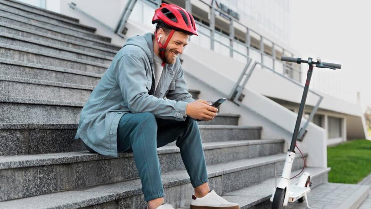Hombre sentado junto a su patinete eléctrico con el casco puesto