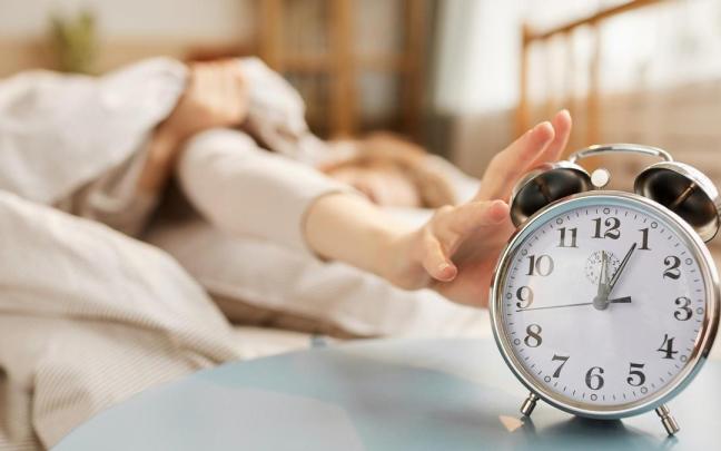 Una mujer estira la mano para apagar el despertador.