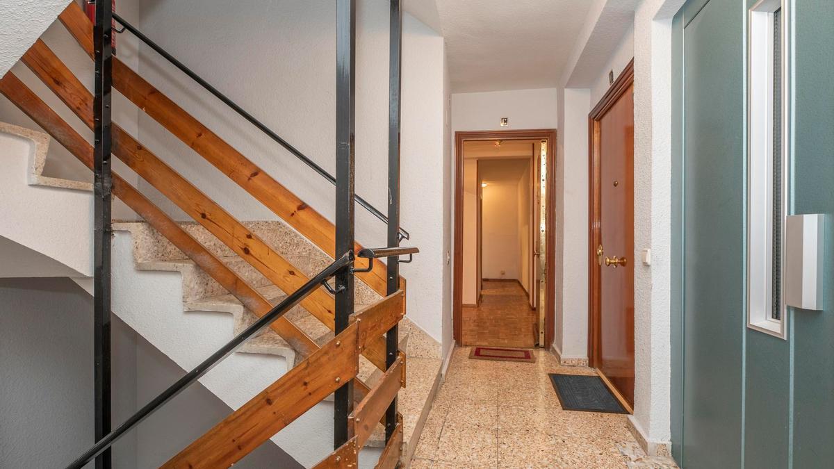 Rellano de escalera con la puerta de una vivienda abierta.