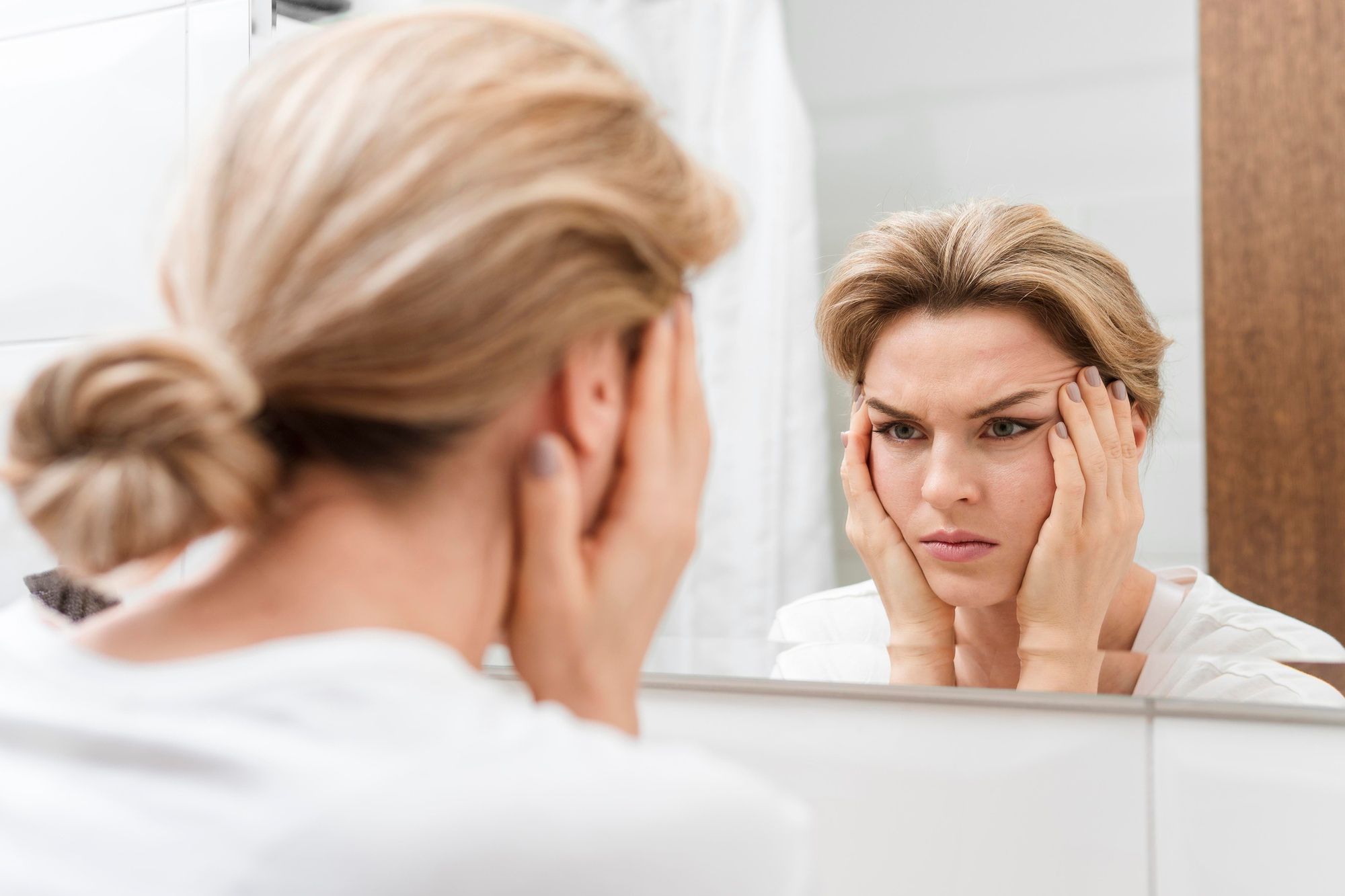 Una mujer se estira la piel del rostro ante un espejo.