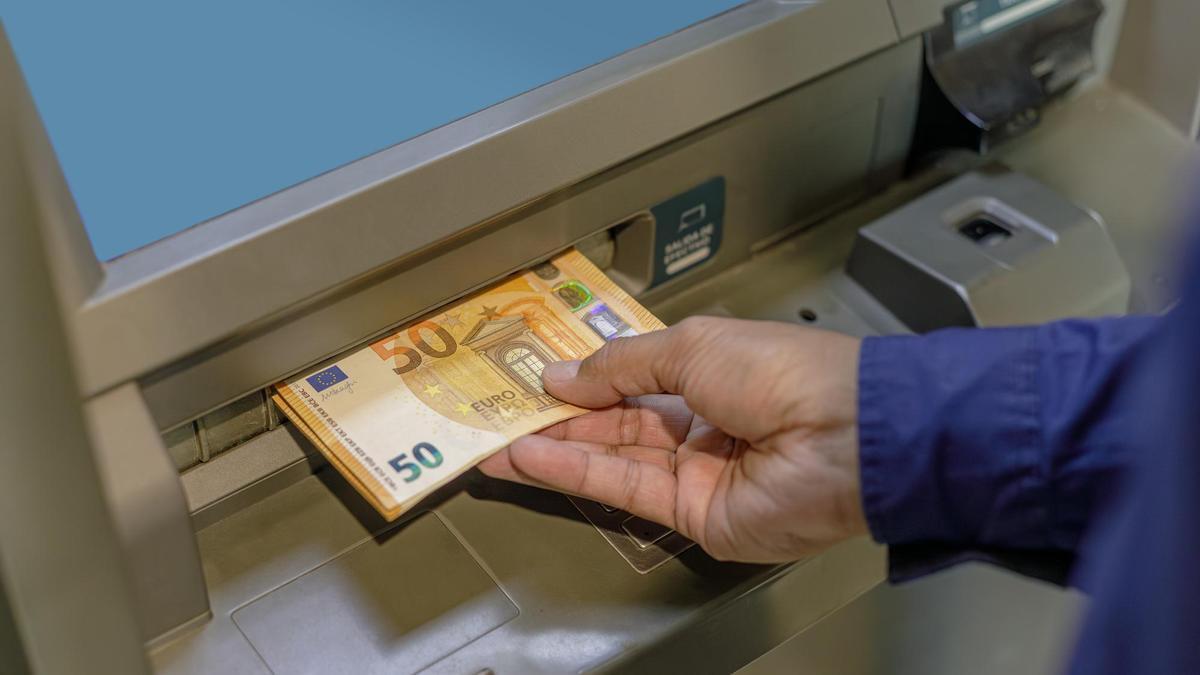 Un hombre introduce varios billetes de 50 euros en un cajero automático.