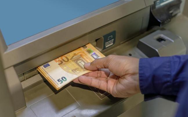 Un hombre introduce varios billetes de 50 euros en un cajero automático. Un hombre introduce varios billetes de 50 euros en un cajero automático.
