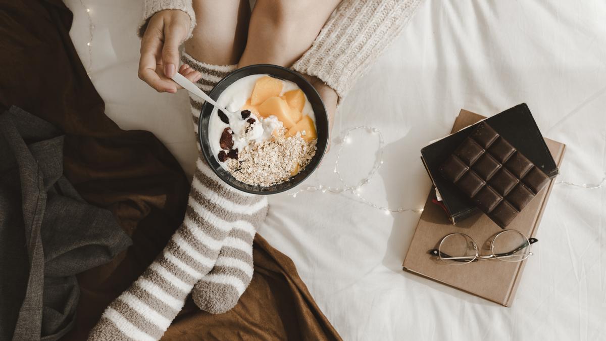 Chica con calcetines toma un bol con cereales y frutas y chocolate negro.