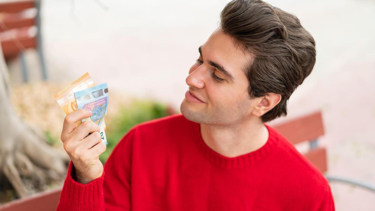 Un joven sostiene en sus manos 70 euros en dos billetes.