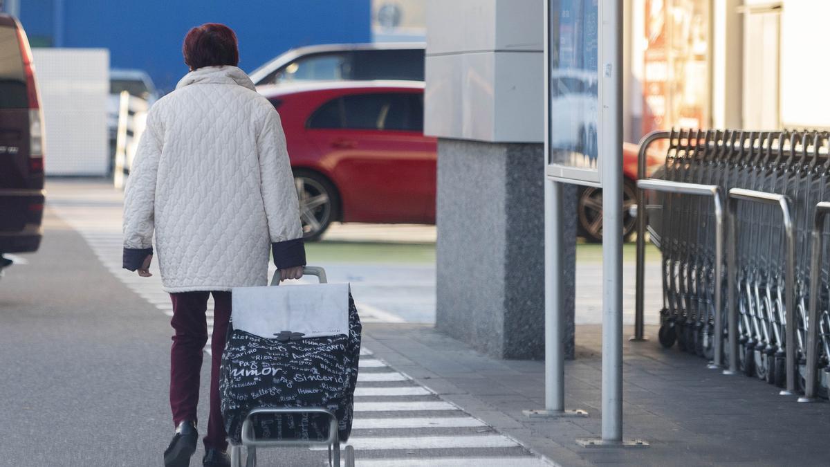 Una mujer sale de un supermercado con un carro de la compra.