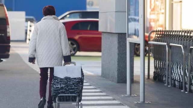 Una mujer sale de un supermercado con un carro de la compra.