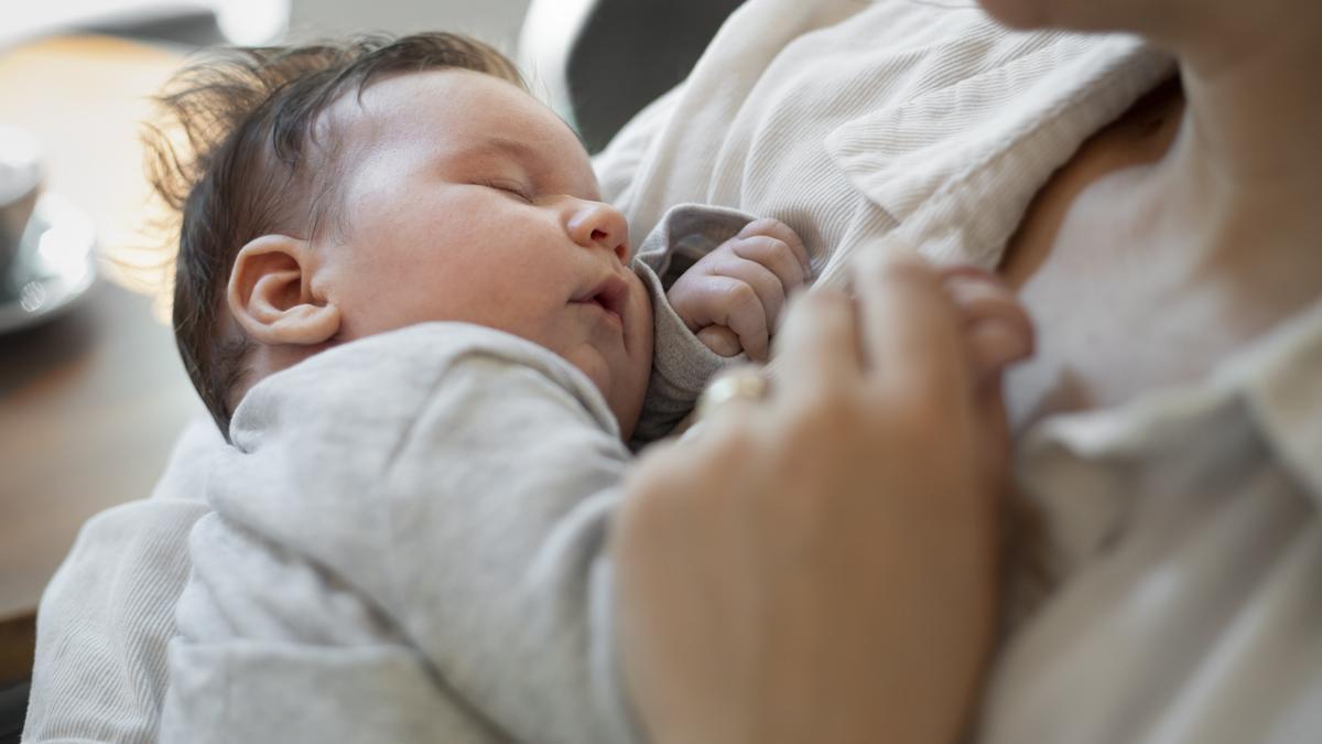 Bebé duerme en brazos de su madre.