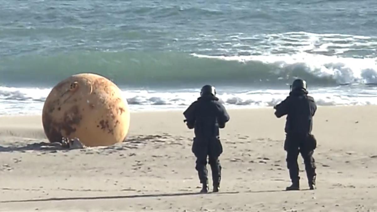 Dos agentes, dispuestos a analizar la enorme bola en la playa japonesa.