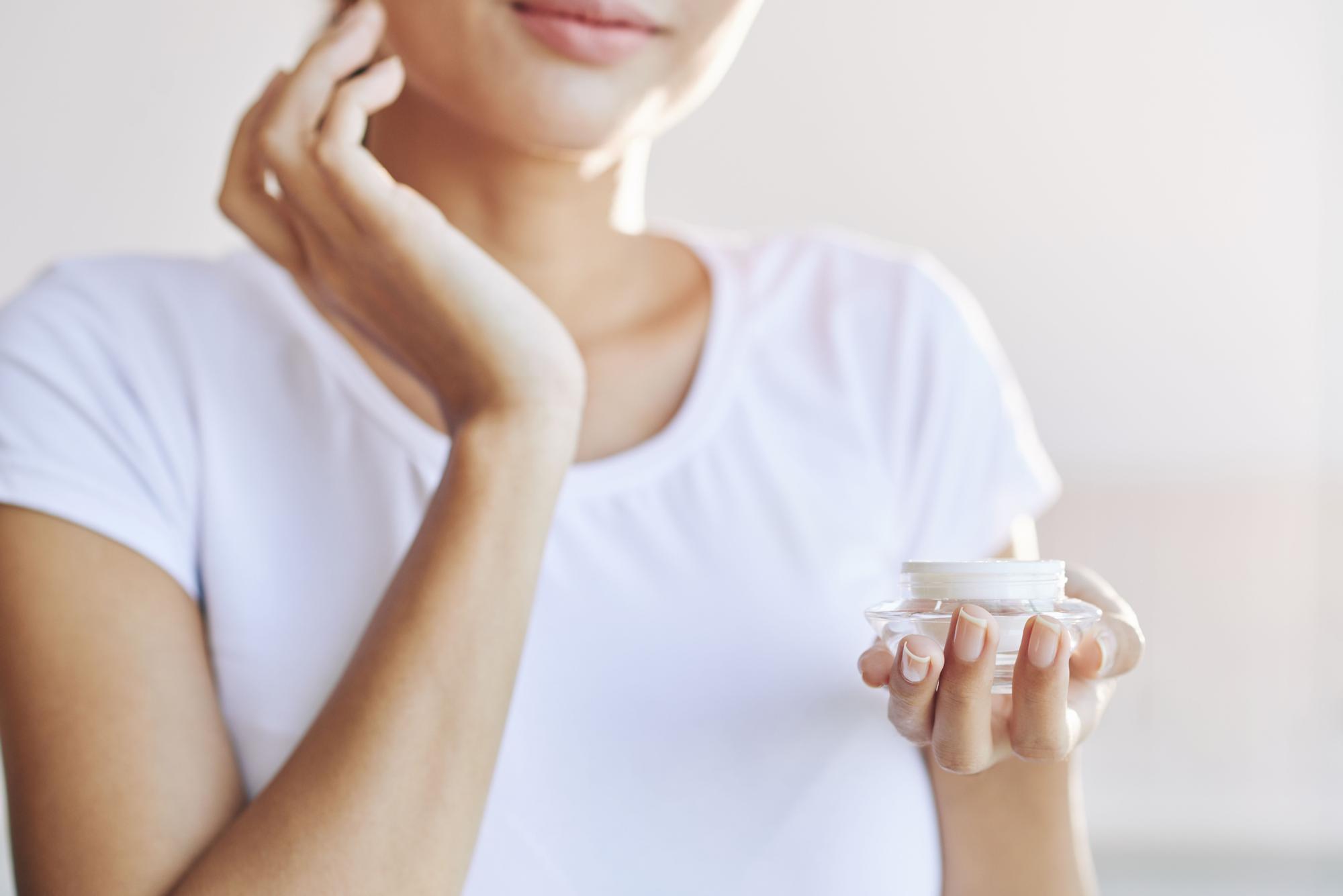 Mujer sostiene un tarro de crema hidratante mientras se la aplica en el rostro como parte de su rutina facial.