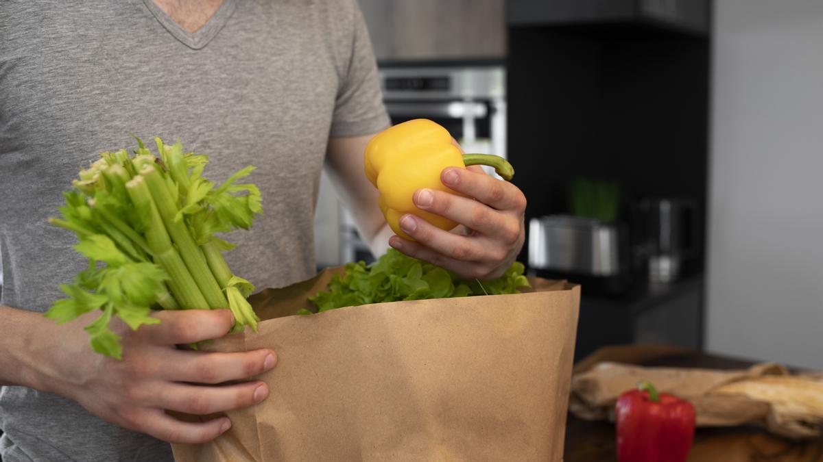 Hombre saca de una bolsa las frutas y verduras que ha comprado en el supermercado