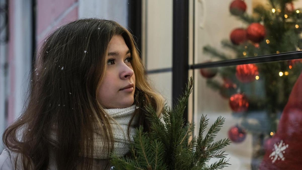 Una joven mira con melancolía un escaparate navideño.