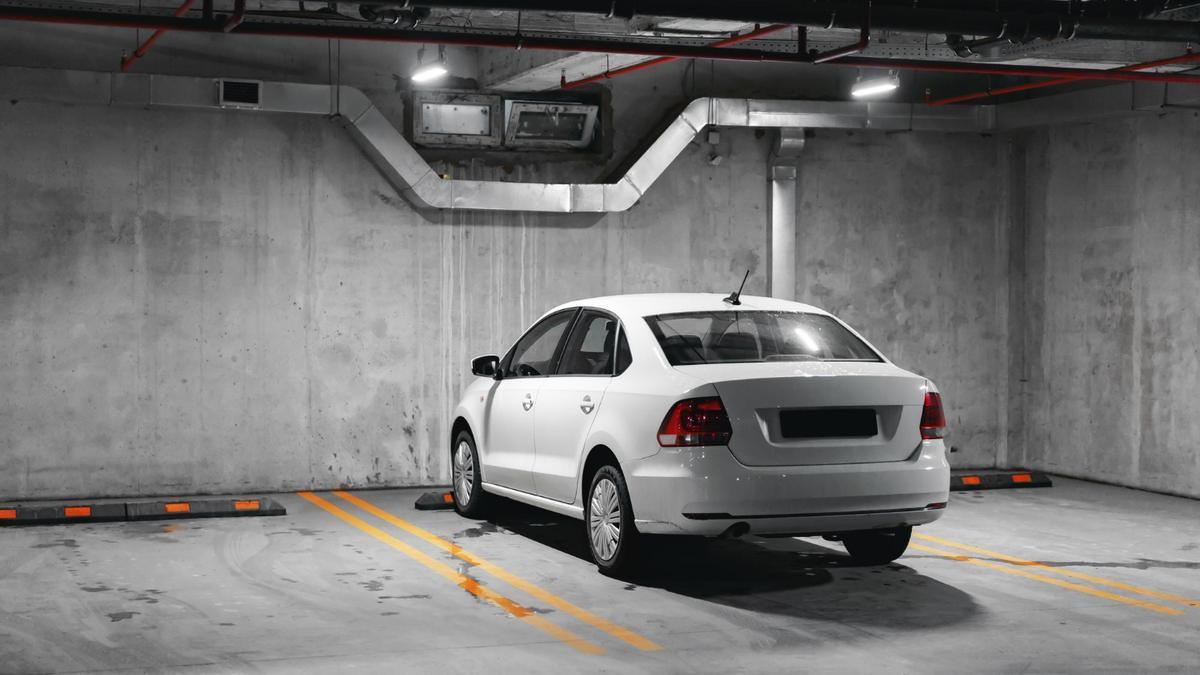 Un coche aparcado en un garaje entre dos plazas vacías.