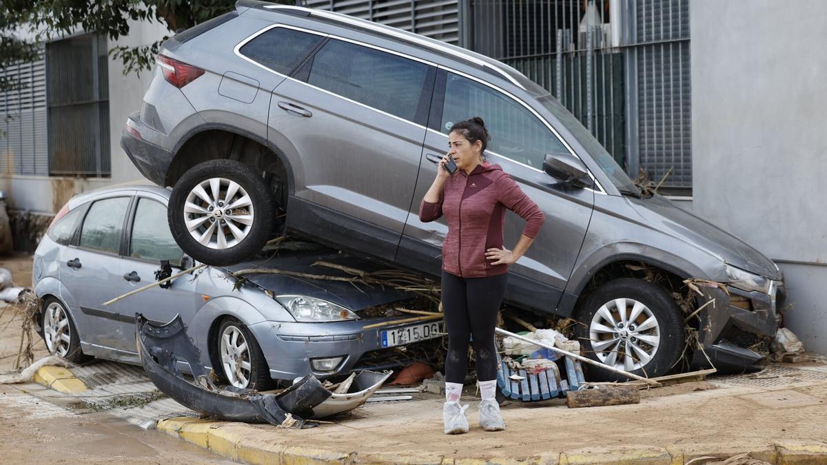 Una vecina de Paiporta habla por teléfono junto a dos coches destrozados tras el paso de la DANA.