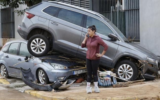 Una vecina de Paiporta habla por teléfono junto a dos coches destrozados tras el paso de la DANA. / Biel Aliño/Efe Una vecina de Paiporta habla por teléfono junto a dos coches destrozados tras el paso de la DANA.