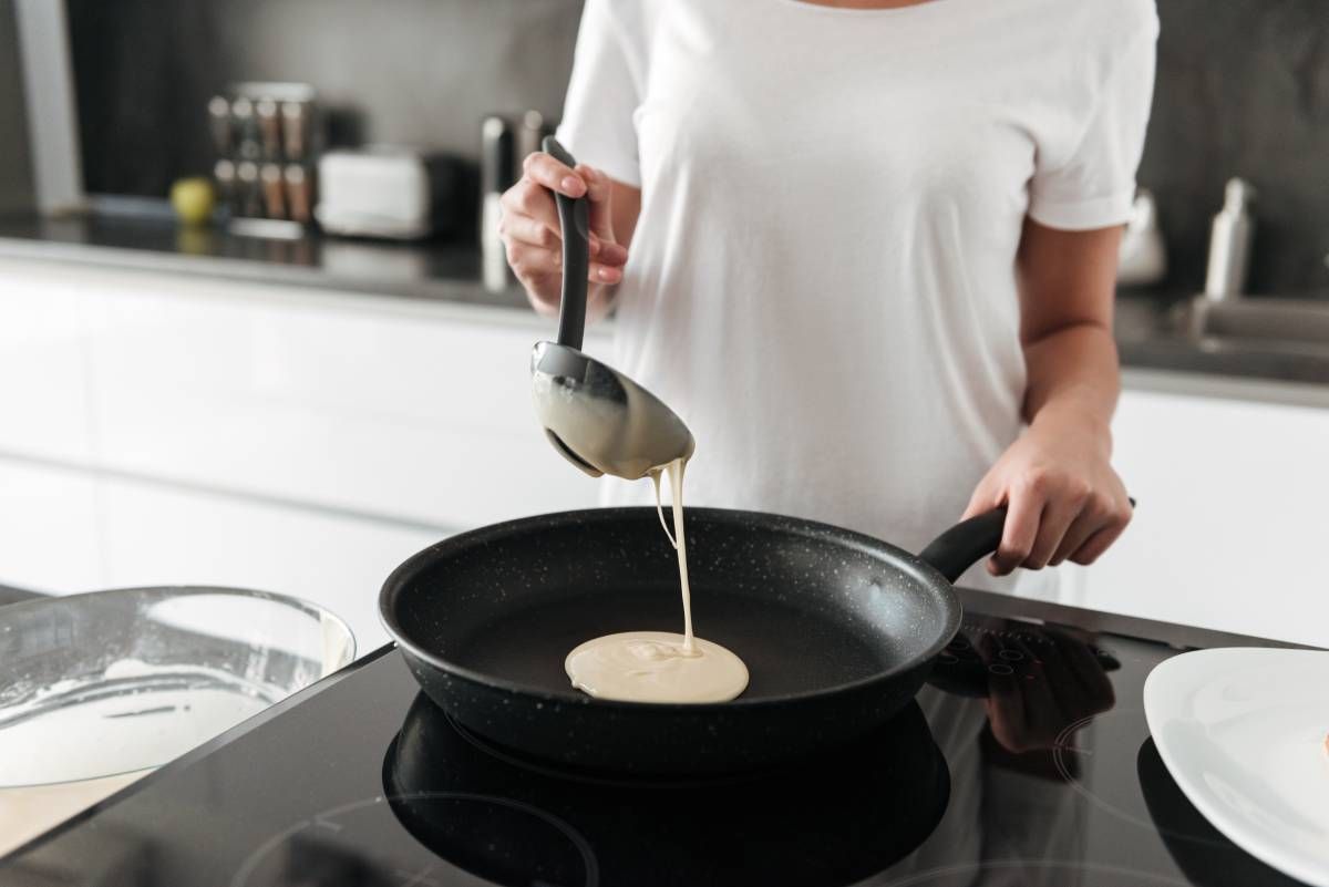Primer plano de una persona cocinando crepes en una sartén antiadherente.