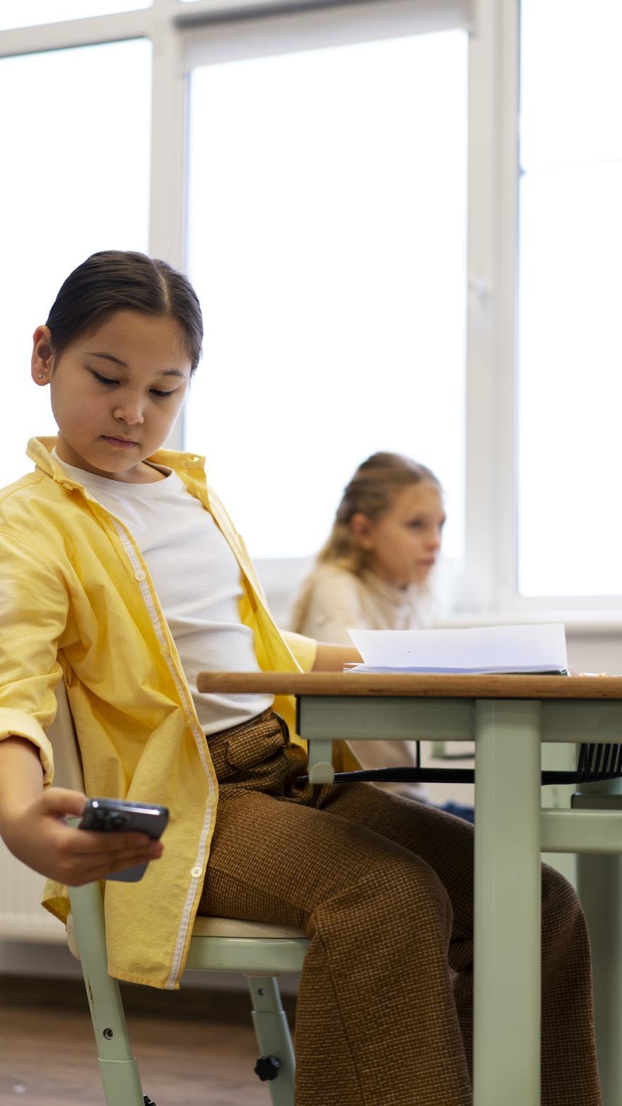 Una nina consulta de forma clandestina su teléfono en un aula.
