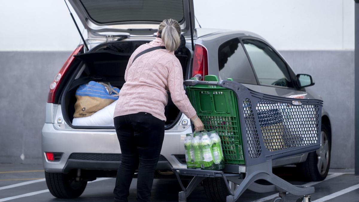Una mujer mete la compra en el maletero de su vehículo.