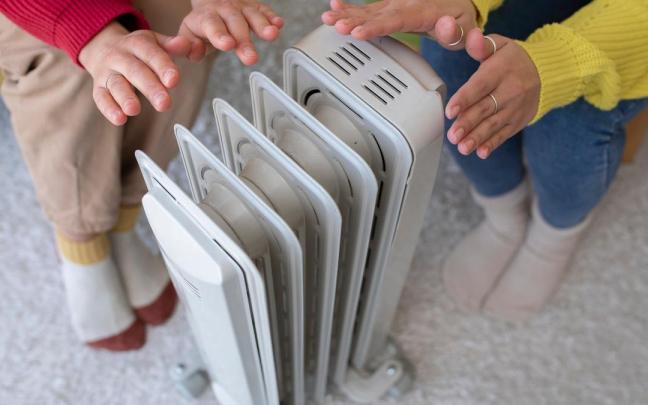 Dos personas se calientan junto a un radiador eléctrico. Dos personas se calientan junto a un radiador eléctrico.