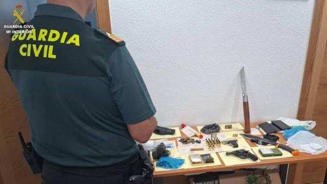 Un agente de la Guardia Civil junto a las armas, la munición y otros efectos intervenidos al detenido.