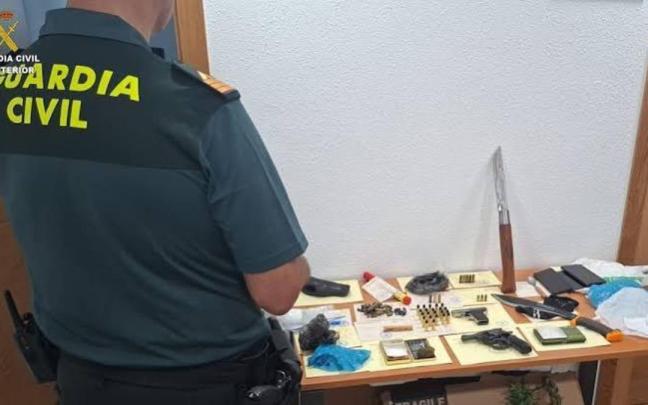 Un agente de la Guardia Civil junto a las armas, la munición y otros efectos intervenidos al detenido.