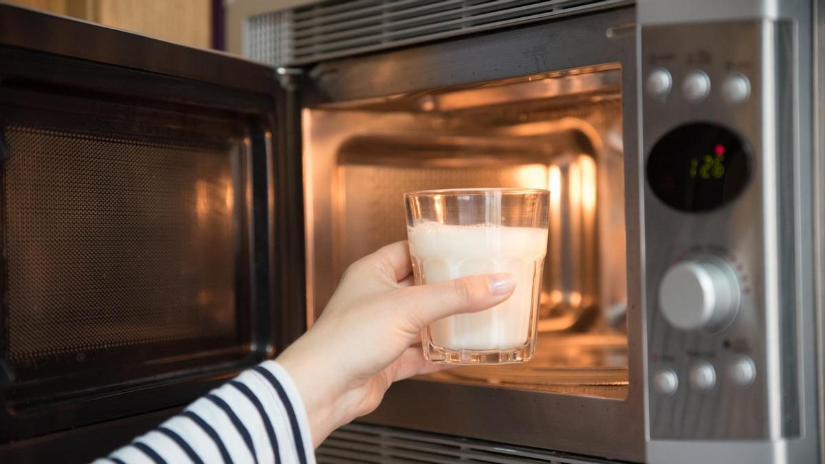 Una mujer mete un vaso de leche en el microondas.