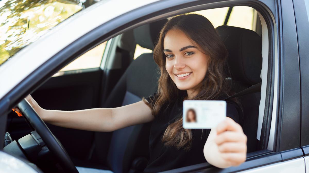 Una joven exhibe sonriente su carnet de conducir desde el interior de su coche.