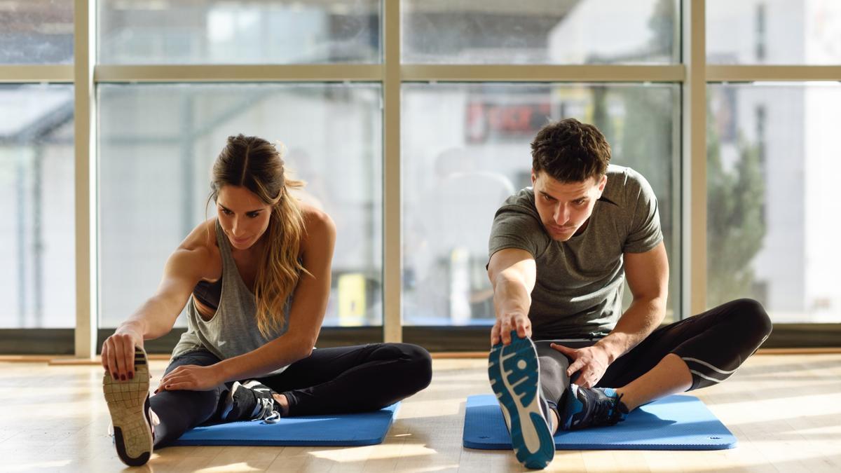 Una mujer y un hombre realizan estiramientos en un gimnasio.