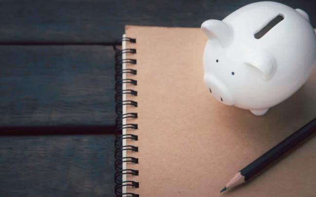Una libreta, un lápiz y una hucha de un cerdito sobre una mesa.