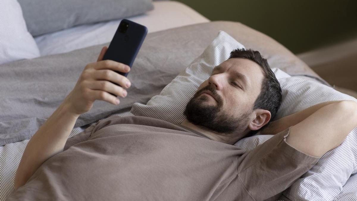 Hombre revisa su móvil desde la cama antes de dormir.