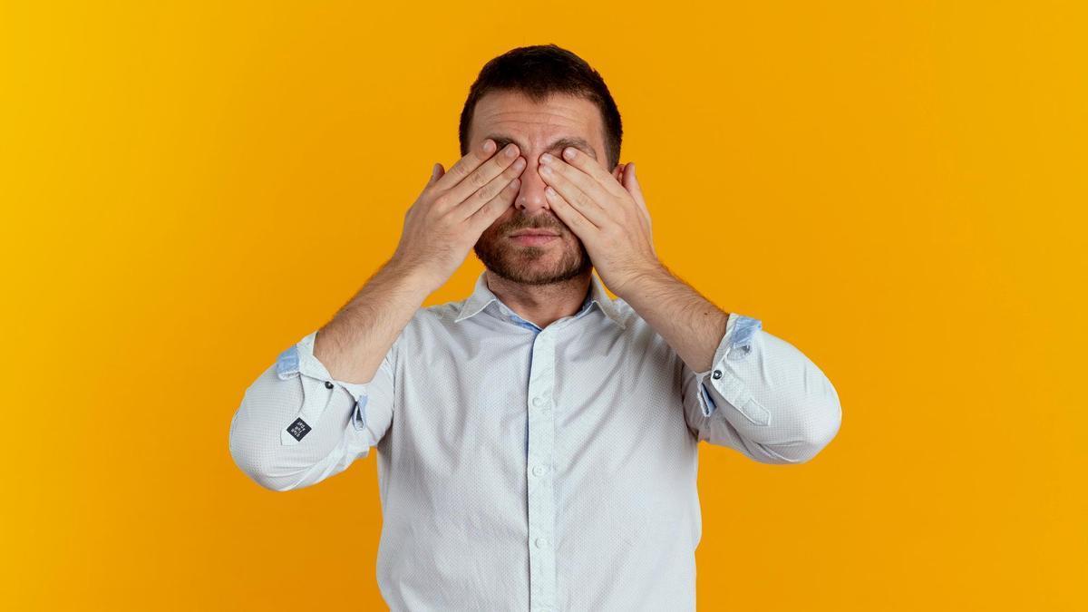 Un hombre se frota los ojos con las manos.