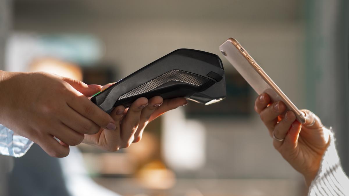 Una mujer paga acercarndo su smartphone a un datafono.