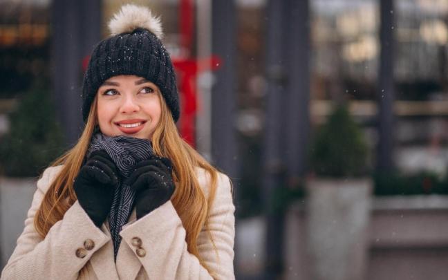 Una mujer pasea por la calle en invierno abrigada con gorro y guantes.