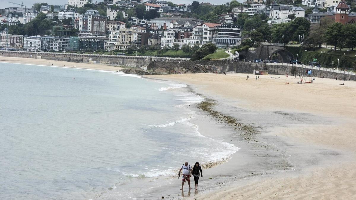 Dos personas pasean por la orilla de la playa donostiarra de Ondarreta