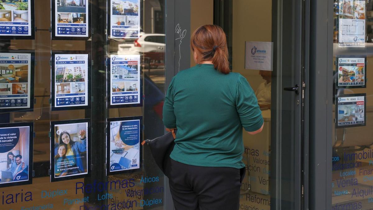 Una mujer pasea junto a una inmobiliaria.