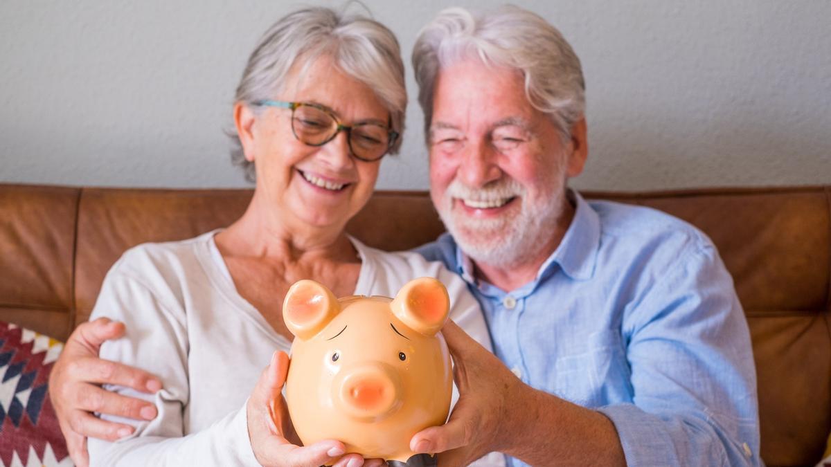 Una pareja de jubilados contempla una hucha con ahorros.