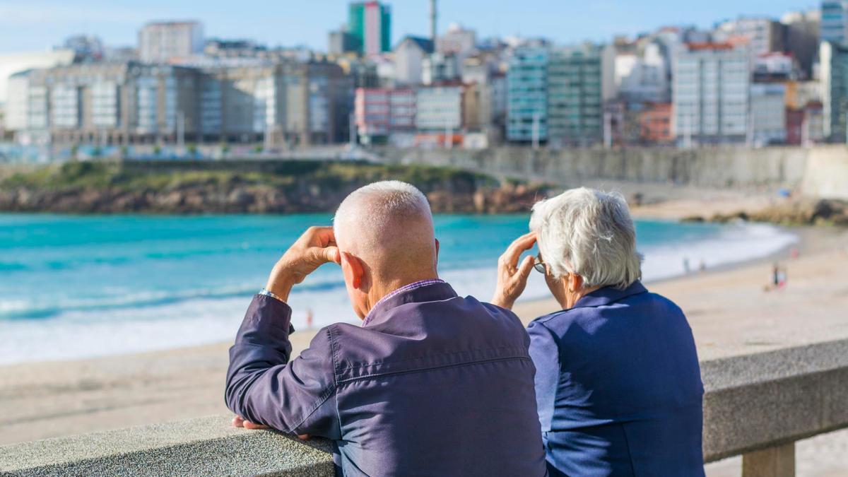 Una pareja de ancianos mira al mar desde un paseo marítimo.