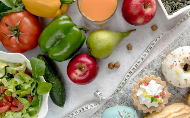 Una cinta métrica separa la comida saludable de los dulces.