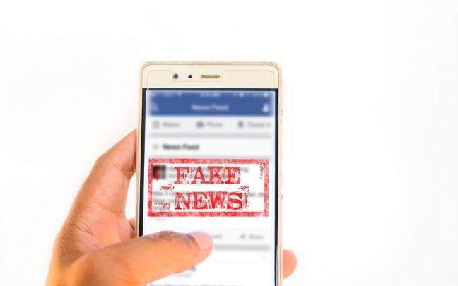 Una persona sujeta un móvil con el sello de 'fake news' en la pantalla. Una persona sujeta un móvil con el sello de 'fake news' en la pantalla.